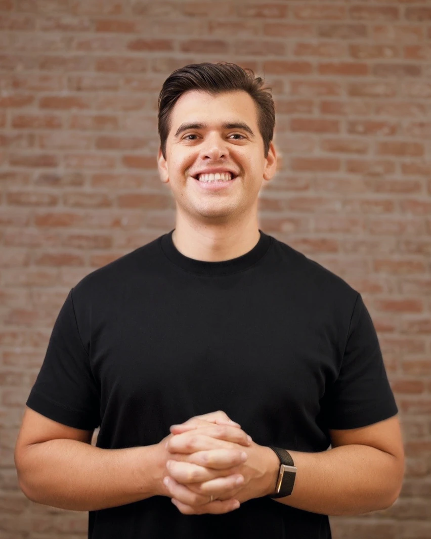 Alberto Fernández smiling with his hands together, in a black t-shirt in front of a brick wall.